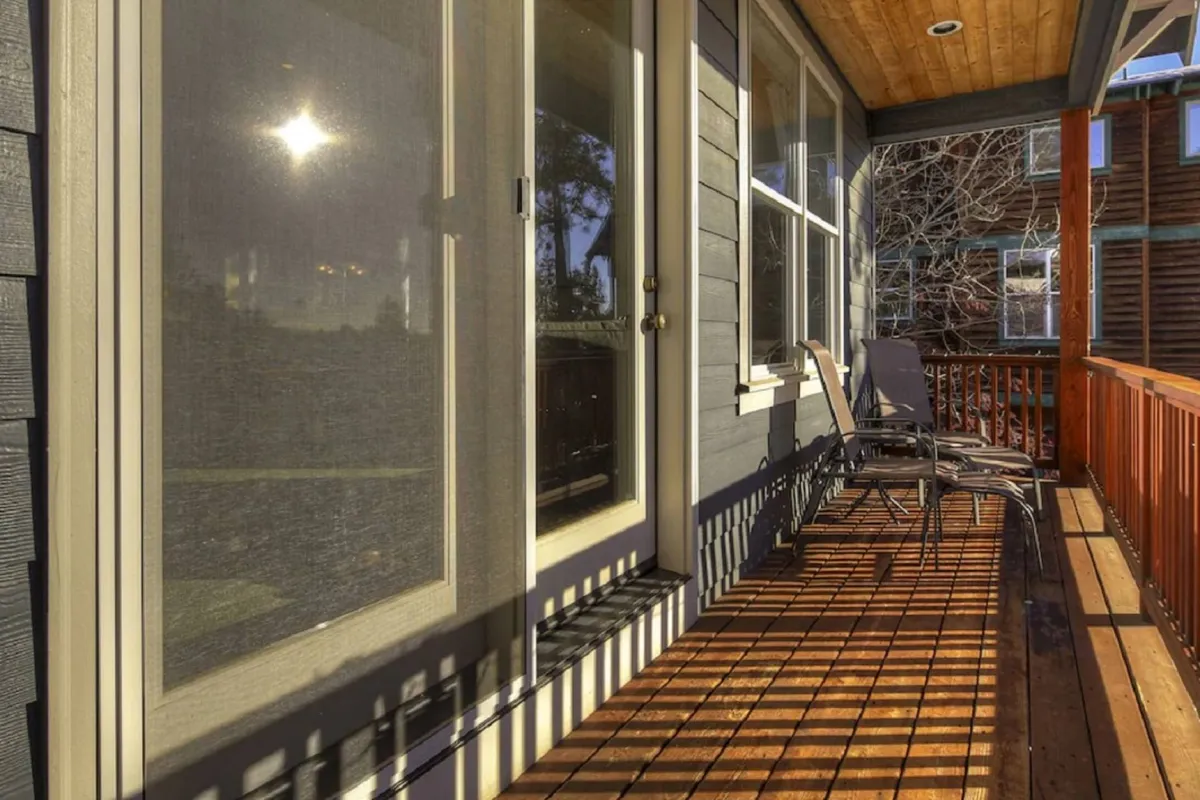 The photo captures a tranquil front deck with inviting chairs positioned near the entryway, perfect for enjoying a cup of coffee while basking in morning sunlight. The clean lines of the deck and the soft natural light highlight the welcoming atmosphere of the home’s entrance.