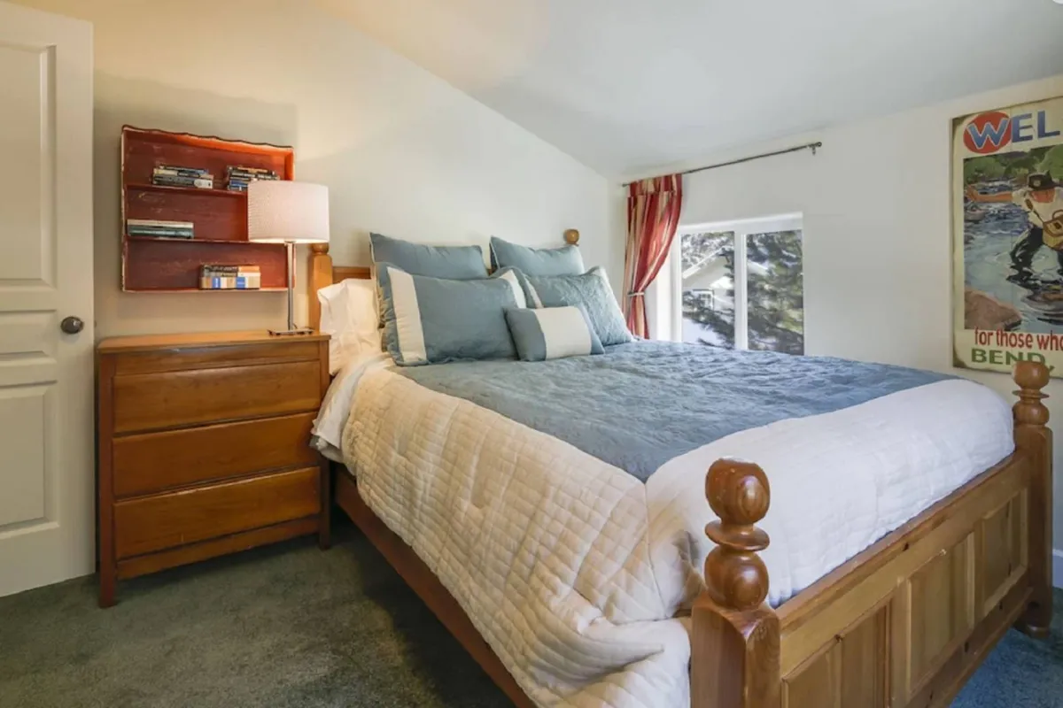 A cozy bedroom with a neatly made bed, shelves, a window letting in gentle light, and a decorative poster. The setting invites relaxation, reading, and quiet behavior, supported by the soft ambiance.
