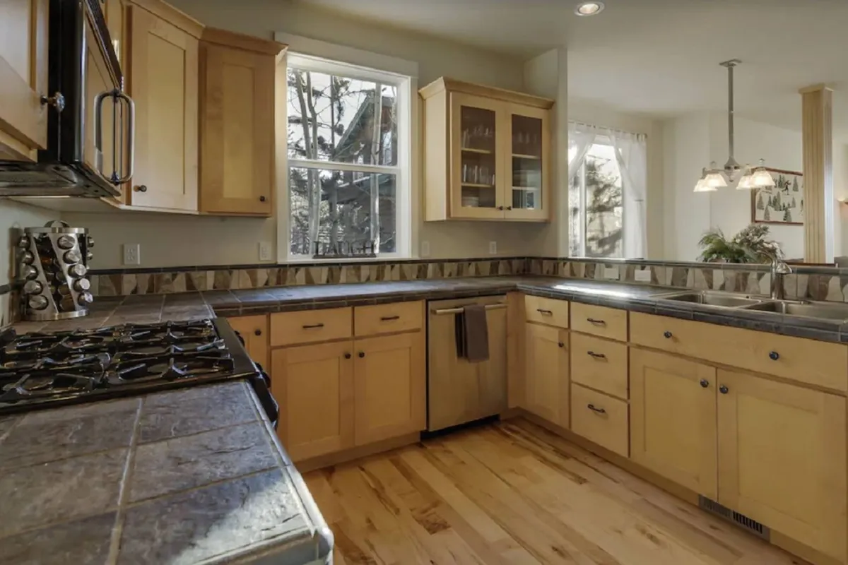 A warm, well-equipped kitchen is the focal point of this image, featuring inviting cabinetry, a neat countertop, and sunlit windows. The space looks ready for meal prep, family gatherings, and sharing recipes.
