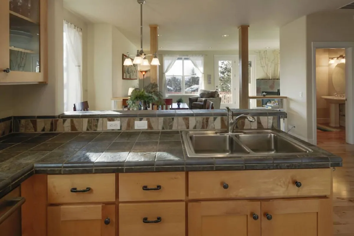 A warm, open-concept layout that provides a view from the kitchen island across the dining area to the living space. The arrangement encourages effortless movement and interaction, with pendant lights, dining space, and cozy seating visible in one inviting sweep.